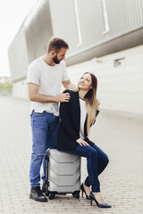 Happy young couple watching airplanes near the airport. A woman sitting on a suitcase. Travel after quarantine. Business trip or vacation trip. A sunny day for airplane flights