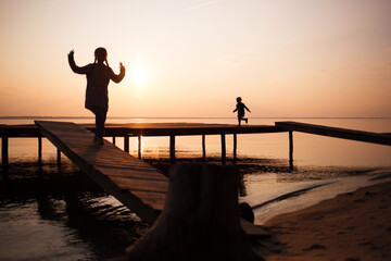 Fototapeta premium silhouettes of people children on shore lake. Summer sunset on water. evening walk outdoor on bridge