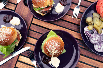 Food on a plate on a table with homemade burger and vegetables. Eating in a garden in summer time outdoors. Gourmet hamburger for eat on lunch. Close up and top view.