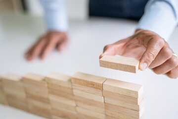 Close up of hand holding small wooden brick put on the wall, Risk and solution.