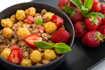 Mueslis with berries in a black  cup on the white table, macro