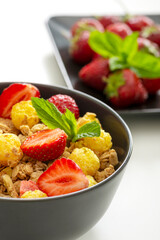 Mueslis with berries in a black  cup on the white table, macro