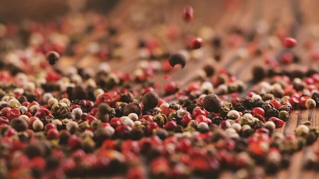 Mixed peppercorns falling on wooden table, heap of spice, mix of different peppers closeup, 240 fps slow motion