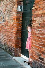 cute little girl wearing a surgical mask is standing up outside her door in Venice Italy