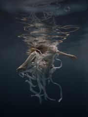 Girl in a dress with ribbons swims underwater