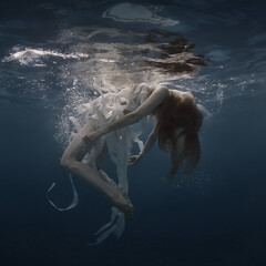 Girl in a dress with ribbons swims underwater