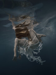 Fototapeta na wymiar Girl in a dress with ribbons swims underwater
