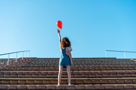 Young woman standing on granstand, letting go of a red ballon