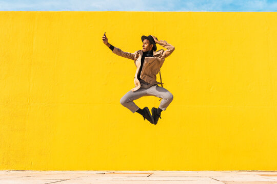 Young man dancing in front of yellow wall, taking selfies