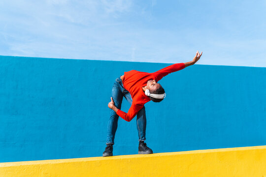 Young man with headphones, listening music, dancing on yellow wall