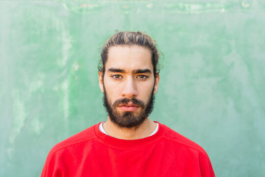 Portrait of bearded young man wearing red sweatshirt in front of green wall