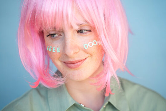 Young woman wearing pink wig, letters on her face, free doom