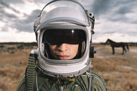 Man posing dressed as an astronaut on a meadow with dramatic clouds in the background