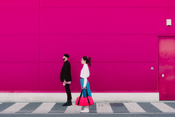 Man and woman standing on a pink wall, looking away