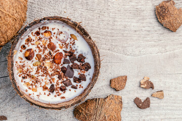 Coconut milk and granola made from oatmeal, nuts,dried fruits and grated chocolate in a coconut shell on a wooden background.Сoncept of healthy food and healthy desserts.Copy space for text