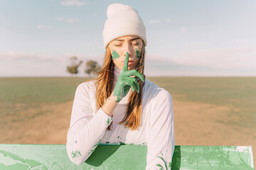Young woman putting finger of green hand on her mouth