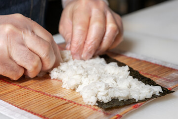 Obraz na płótnie Canvas Sushi chef wearing gloves lays the rice on the nori