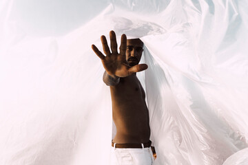 Barechested young man inside a plastic foil raising his hand