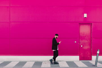 Businessman using smartphone and walking along a pink wall