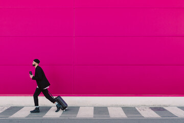 Young man with trolley walking along a pink wall, holding reusable cup