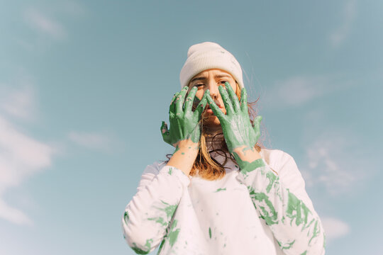 Young woman holding green painted hands in front of her face