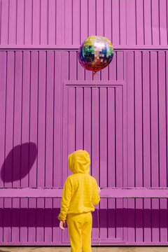 Back view of children dressed in yellow holding balloon in front of purple background