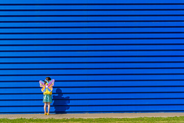 Back view of little girl with colourful butterfly wings standing in front of blue background