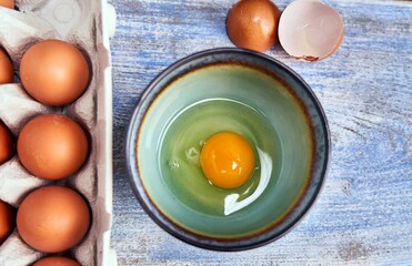 Top view of raw egg in bowl, eggshell and egg box on colorful background. Concepts of preparing for breakfast, cooking at home.