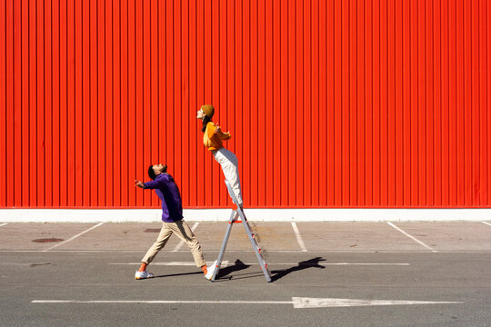 Young man and woman performing with a ladder in front of a red wall