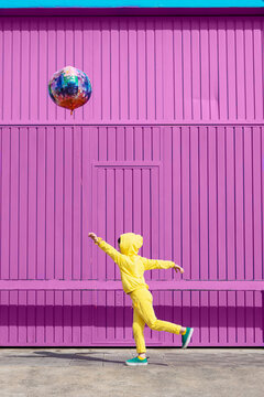 Children dressed in yellow standing in  front of purple garage door holding balloon