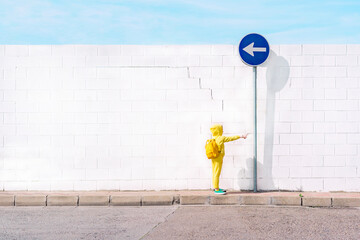 Girl with her toy on a traffic sign, direction left in front of a white wall