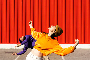 Young man and woman performing on road in front of red wall
