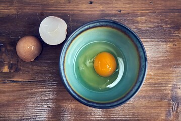 Top view of raw egg in bowl, eggshell on brown wooden table. Concepts of preparing for breakfast, cooking at home.