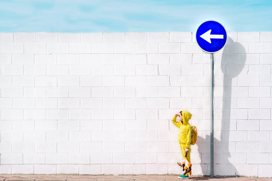 Girl with her cuddly toy at traffic sign, direction left, in front of a white wall