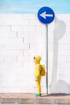 Girl standing on a traffic sign, direction left, in front of a white wall