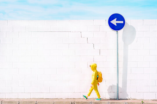 Girl walking at a traffic sign, direction left in front of a white wall
