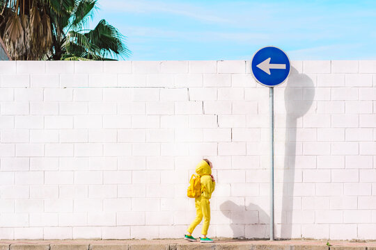 Girl looking at traffic sign, direction left, in front of a white wall