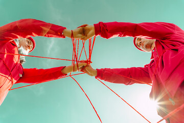 Directly below view of couple performing with red string against sky