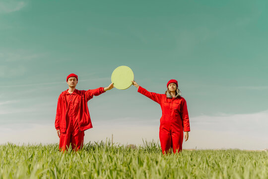 Young couple wearing red overalls  standing on a field holding green circle