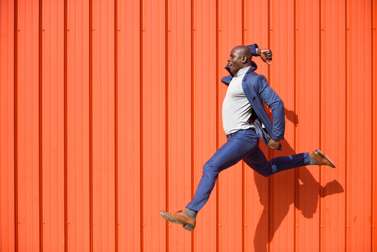 Businessman jumping in the air in front of orange wall