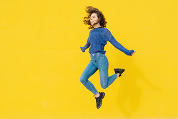Young woman jumping in the air in front of yellow background