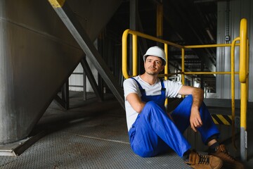 Fototapeta na wymiar Young smiling professional in overalls and protective helmet standing in front of camera inside large machinebuilding plant