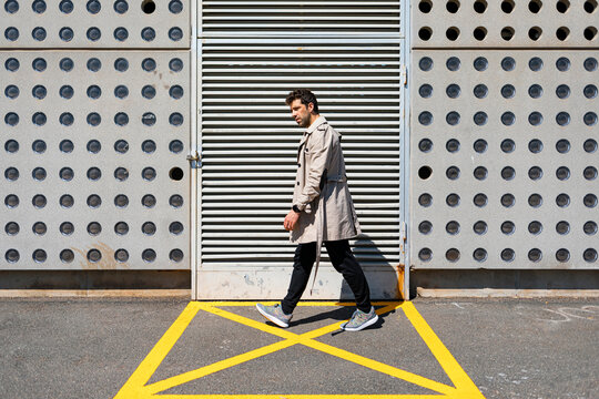 Impatient man walking in yellow marked area in front of concrete wall
