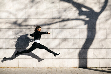 Young woman making a big jump on a  wall with a shadow of a tree