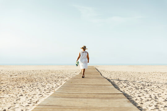 Senior woman walking on boardwalk on the beach, El Roc de Sant Gaieta, Spain
