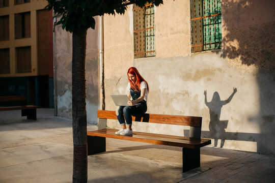 Redheaded woman sitting on bench using laptop