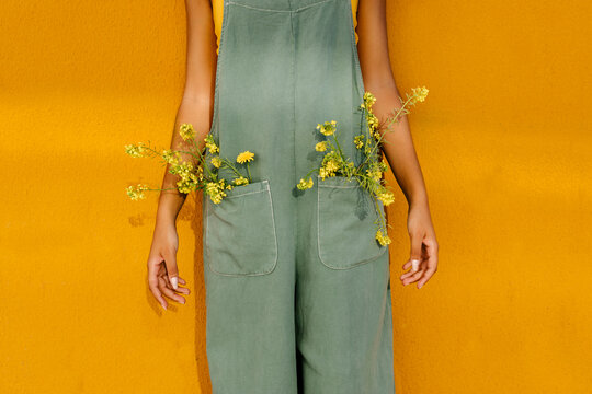 Midsection of woman wearing overalls with yellow flowers in pockets