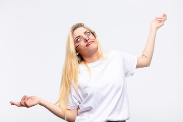 young pretty blonde woman shrugging with a dumb, crazy, confused, puzzled expression, feeling...