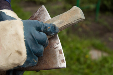 A man in gloves sharpens an iron axe with a special knife stone. A place for inscription.