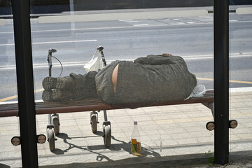 Homeless man is sleeping on a bench at the bus stop